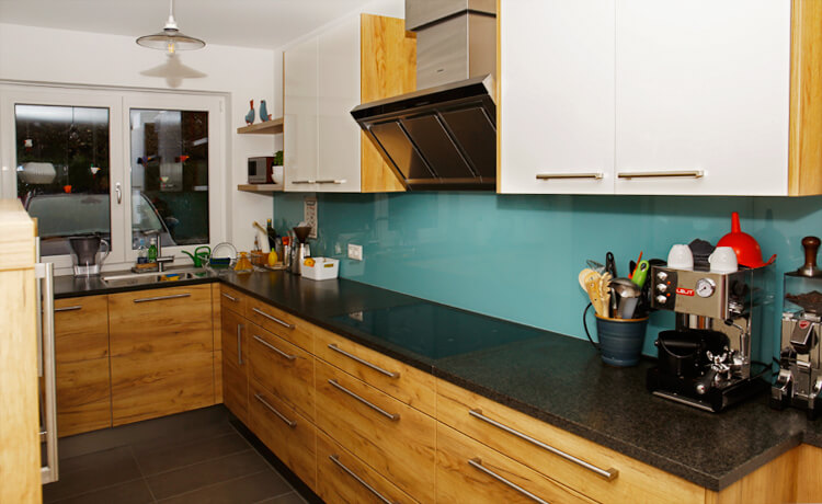 Die türkisblaue Rückwand aus Glas und die Maserung des Holzes macht Stimmung in dieser Küche